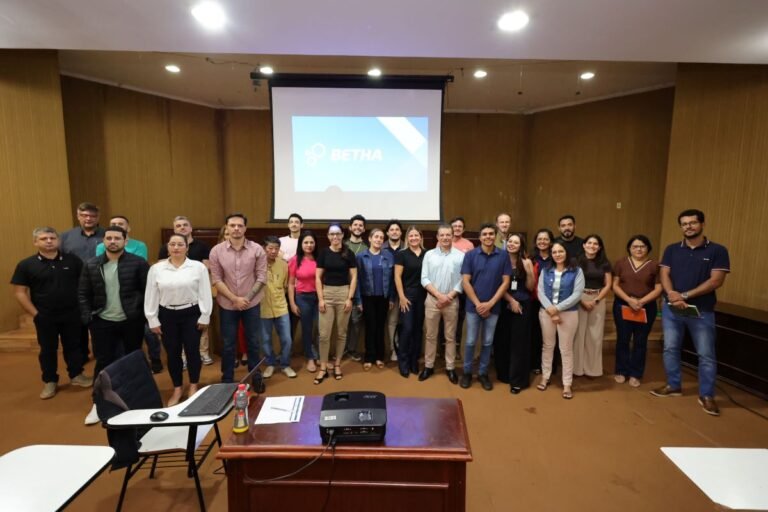 About 25 people stand in a conference room in front of a projector screen displaying the BETHA logo, posing for a group photo.