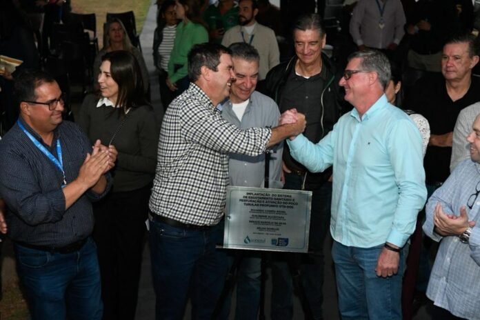 Group of men celebrate at an awards event; two center men shake hands while others applaud, a plaque hangs between them.
