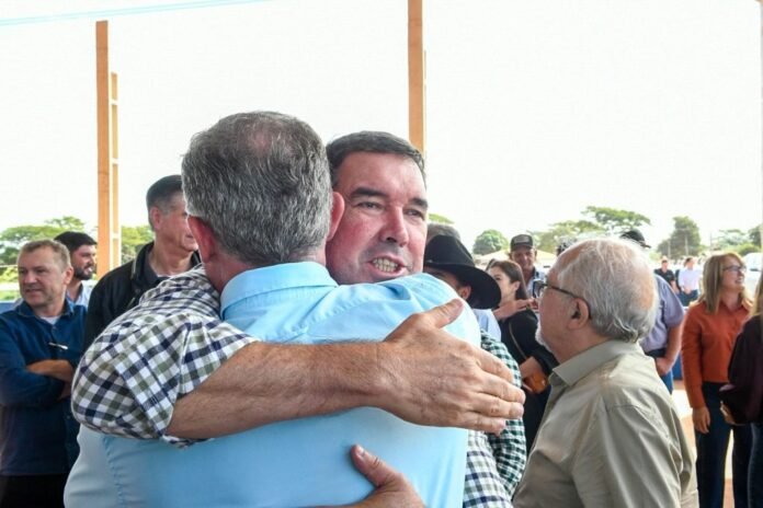 Two men hug in a crowd at an outdoor event, with several onlookers nearby.