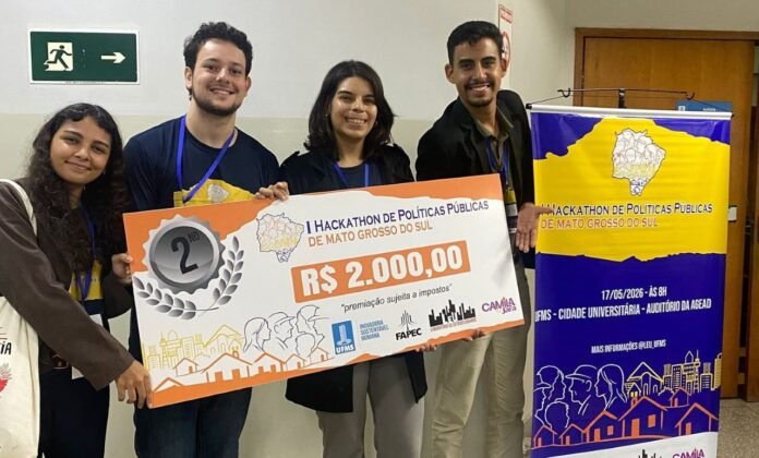 Four young people pose with a large prize check reading R$2.000,00, second place at a Hackathon de Políticas Públicas, backdrop includes event banner.