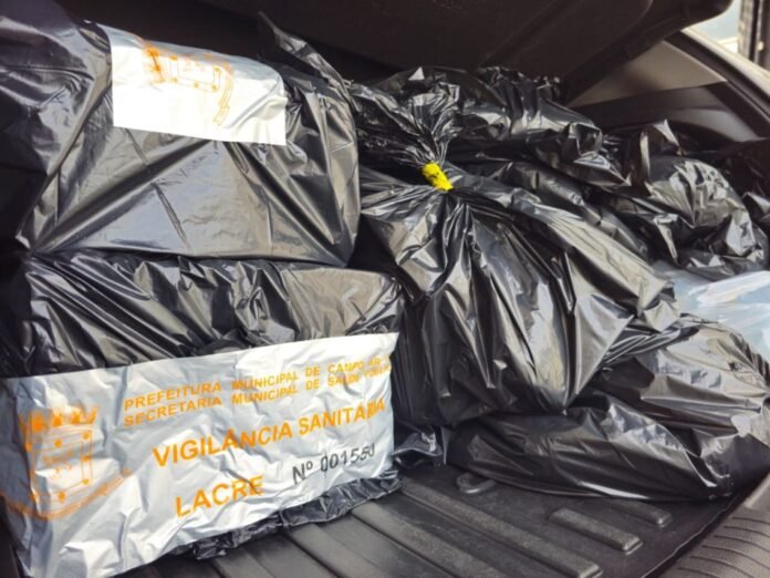 Trunk of a car filled with large black trash bags, including a white label with orange text reading ‘Vigilancia Sanitaria’ and other municipal words.