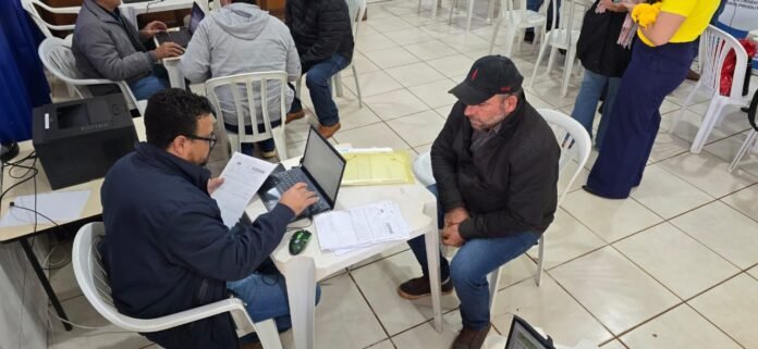 Worker assists a man with documents at a small table; laptop and papers open amid a busy service center.