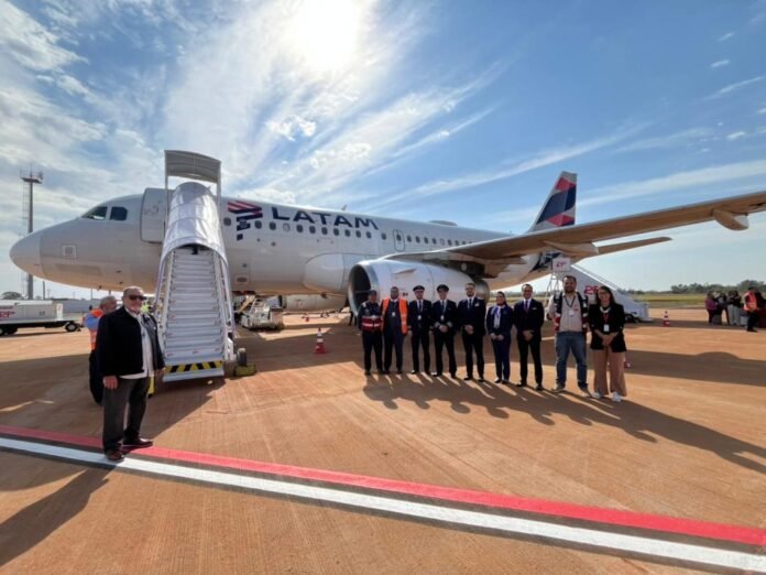 Group of staff and pilots posing beside a LATAM aircraft on the sunlit tarmac with a mobile stairway nearby.