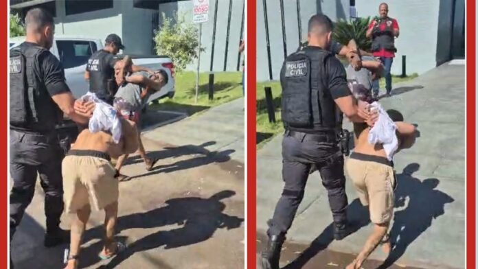 Two police officers in tactical vests restrain a shirtless man outside a building during an arrest.