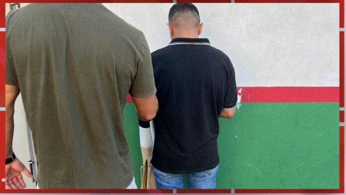 Two men shown from behind standing side by side, facing a wall painted with white, red, and green horizontal stripes.