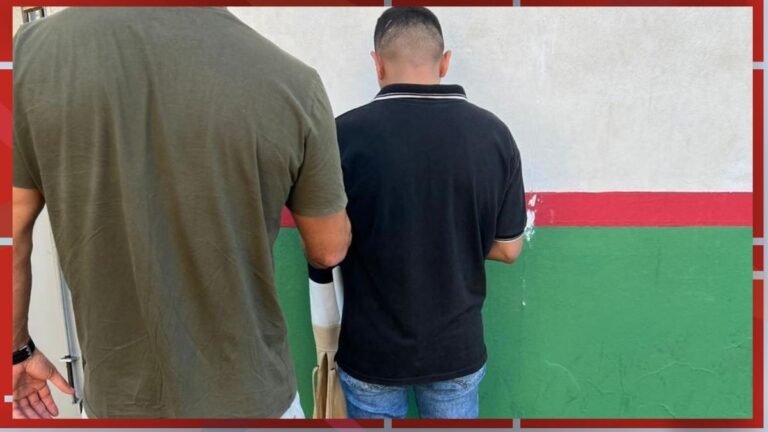 Two men shown from behind standing side by side, facing a wall painted with white, red, and green horizontal stripes.