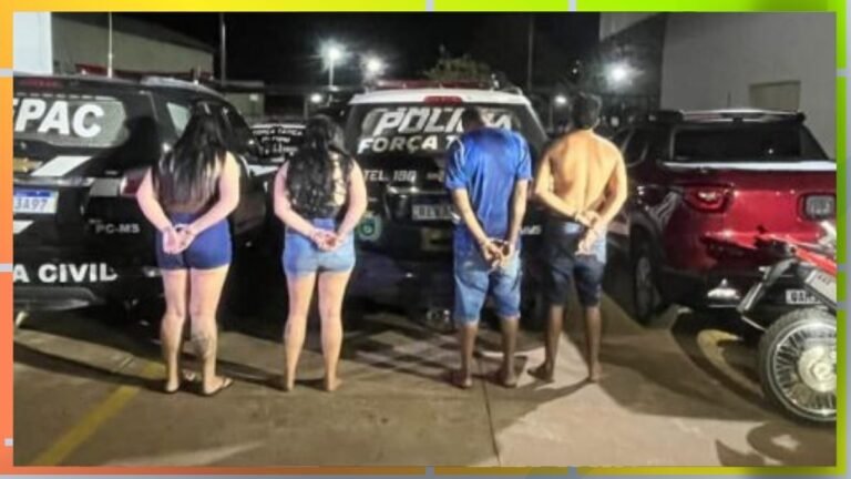 Four individuals stand with hands behind their backs in a dimly lit parking lot beside police vehicles at night.