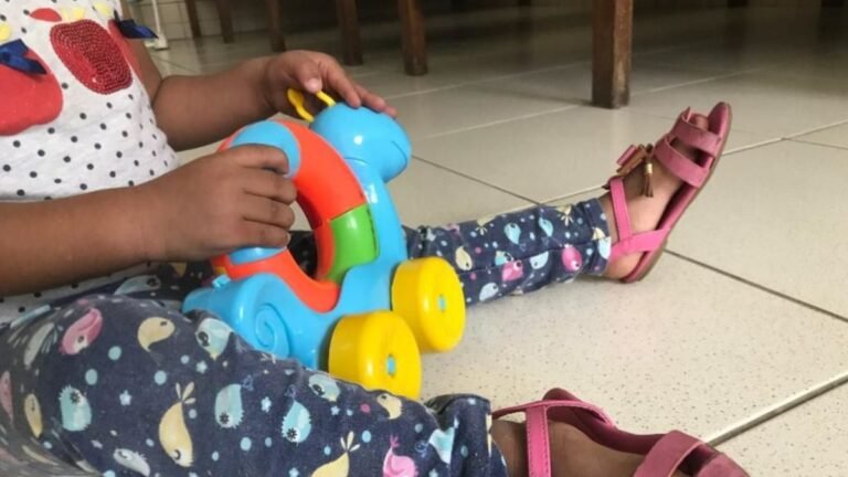 Child sitting on a tiled floor, playing with a colorful plastic toy vehicle steering wheel.