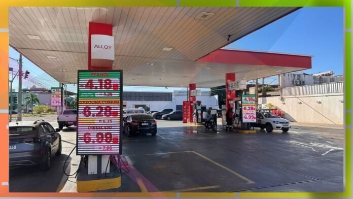 Gas station with price boards and cars refueling under a white canopy on a sunny day
