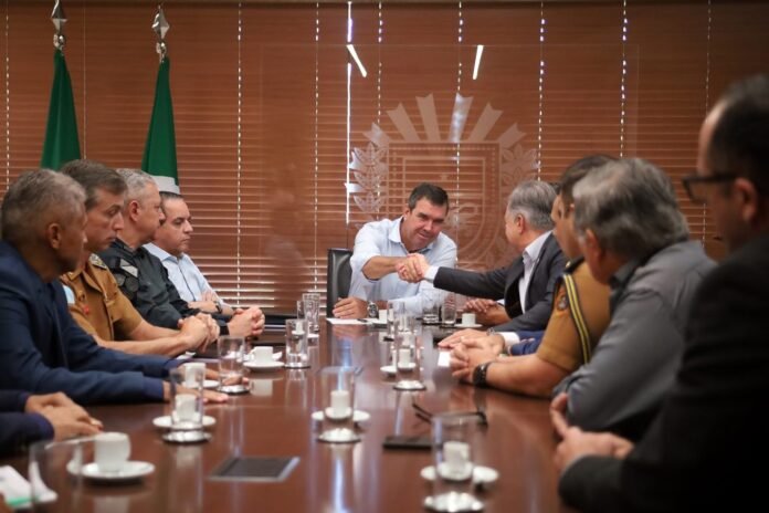 Officials around a long conference table; two men in the center shake hands as others look on.