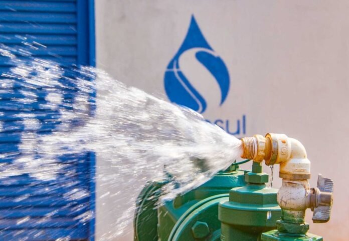 Close-up of a green industrial valve releasing a high-pressure water jet to the left, against a blue and white background with a logo.