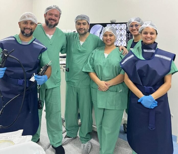 Group of six medical professionals in scrubs and protective gear posing in a hospital room.