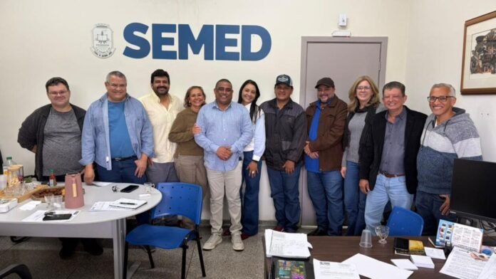 Diverse group of professionals posing for a photo in a conference room with 'SEMED' on the wall; items and papers on the table in front of them.