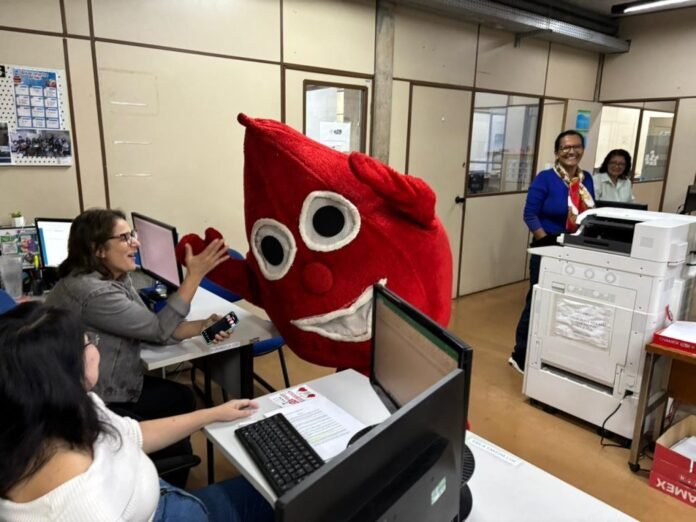 Red plush heart mascot high-fiving a woman at a desk in an office setting