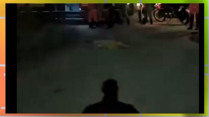 Silhouette of a person seen from behind at night, facing a group of people and motorcycles on a dim street.