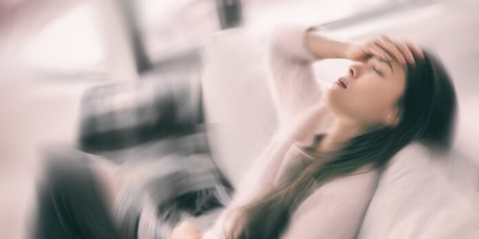 Woman with long hair rests on a couch, hand on her forehead, eyes closed in apparent fatigue or pain