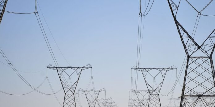 Tall metal transmission towers and high-voltage power lines stretch into the distance against a clear blue sky.