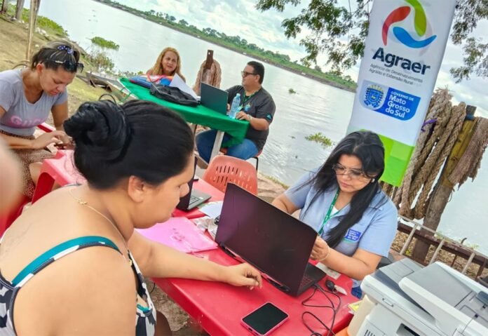 Outdoor lakeside workshop with people at a red table using laptops; banner with Agraer logos in the background.