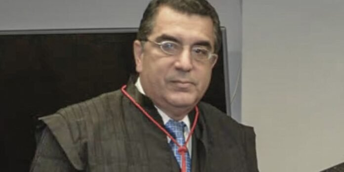 Man wearing a dark academic robe with a red cord around his neck, looking at the camera.