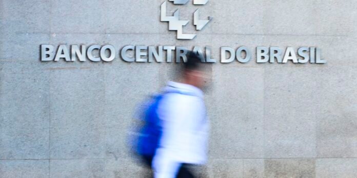 Blurred passerby with a blue backpack walking in front of the Banco Central do Brasil sign on a grey stone wall