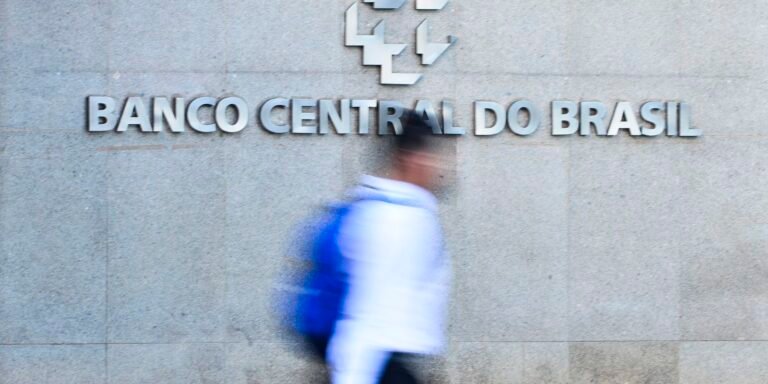 Blurred passerby with a blue backpack walking in front of the Banco Central do Brasil sign on a grey stone wall