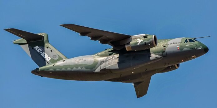 Side view of a green-gray Embraer KC-390 aircraft in flight, Força Aérea Brasileira markings against a clear blue sky.