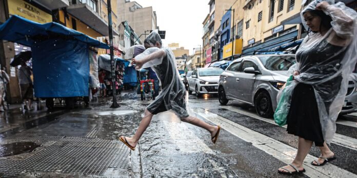 Person in a clear rain poncho mid-leap across a wet city street, with market stalls and cars in the background.