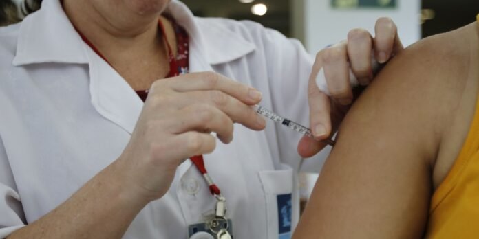 Nurse administers a vaccine to a patient's upper arm, using a syringe and alcohol wipe.