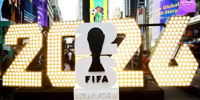 Large illuminated 2023 sculpture with a black FIFA silhouette in Times Square, New York, surrounded by bright billboards and people.