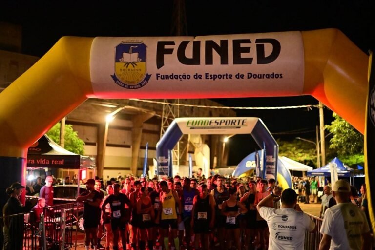 Nighttime race start under a yellow inflatable arch reading FUNED, with runners lined up at the starting line.
