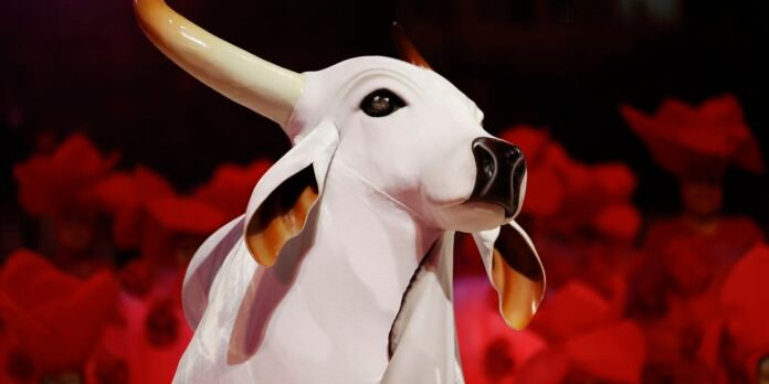 Close-up of a white cow sculpture with large horns and dark nose, set against a vivid red floral background.