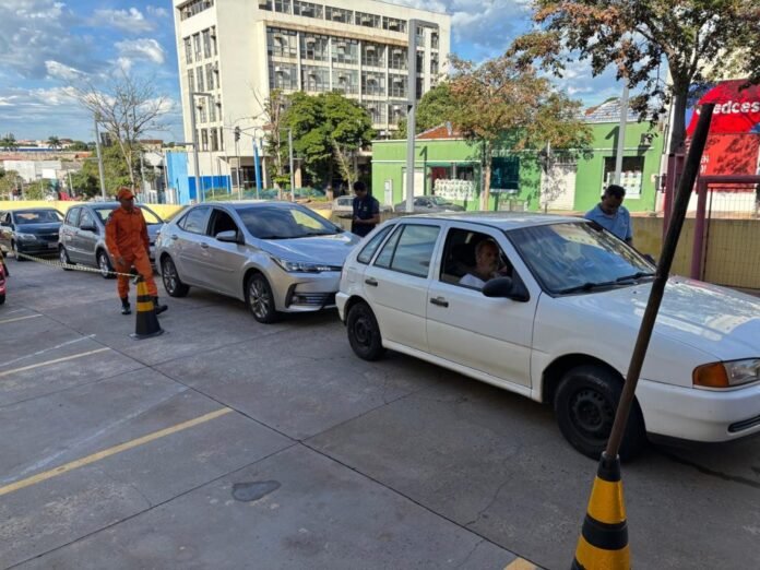 Vehicles lined up in a parking lot as a worker in orange uniform directs traffic with cones nearby.