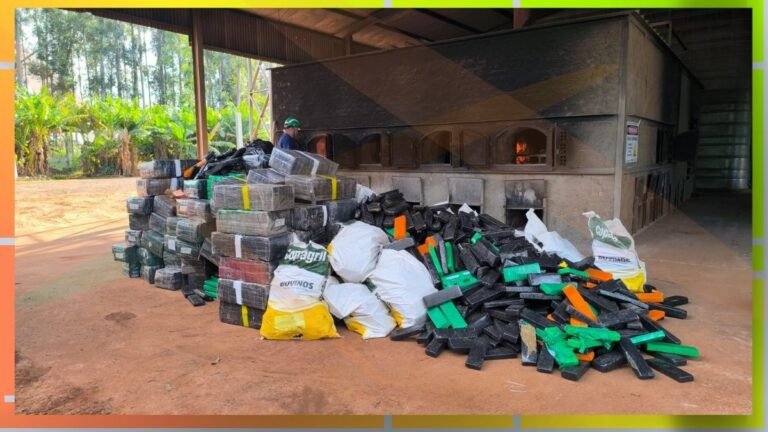 Piles of black and green plastic blocks and white bags stacked outside a large industrial kiln; a worker in a hard hat nearby under a covered area.
