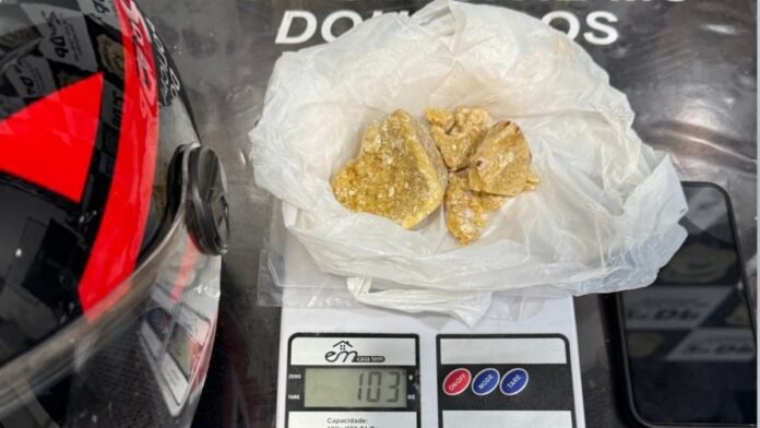 Brown chunky substance in a plastic bag resting on a digital kitchen scale showing 103 g
