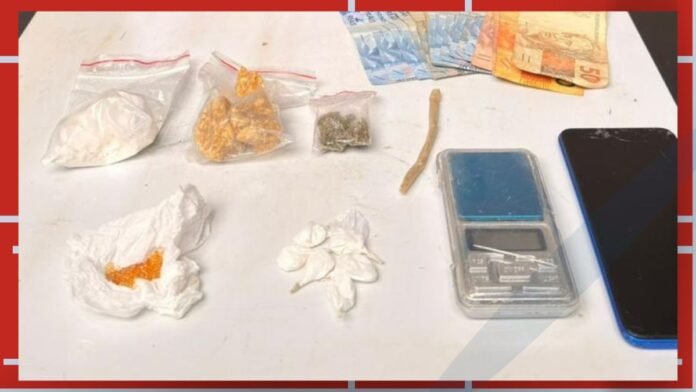 Assorted drug paraphernalia on a table: baggies with white powder, pills, a small scale, cash, and a phone.