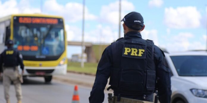Policeman wearing a PRF vest at a roadside checkpoint with a yellow bus and a car in the background.