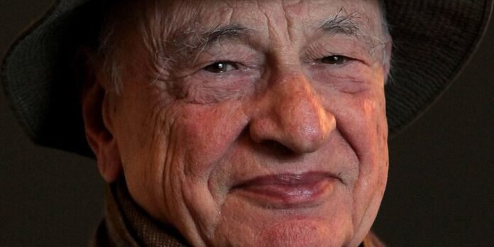 Close-up portrait of an elderly man wearing a hat, smiling with visible facial wrinkles.