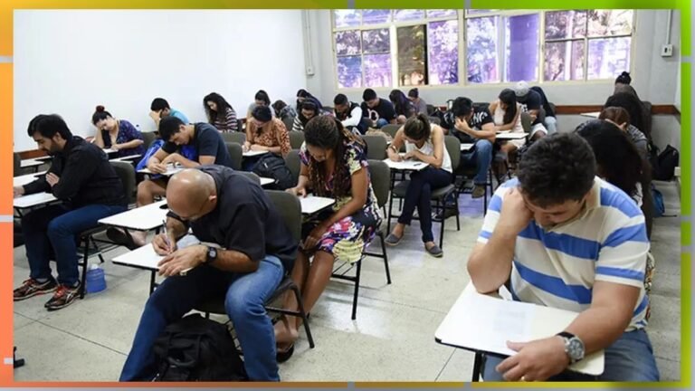 Students seated in a classroom taking a written exam, heads down as they write on papers at their desks.