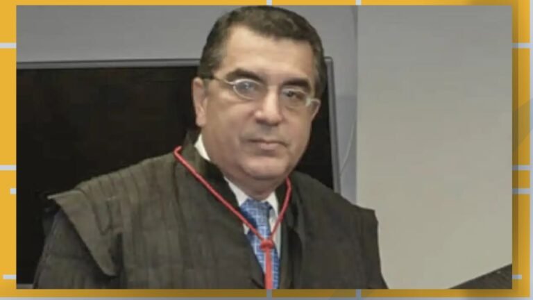 Man wearing a dark academic gown and blue tie, looking at the camera in a formal setting