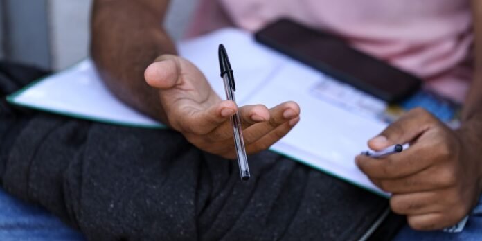 Close-up of a person holding a transparent pen over a notebook resting on their lap, ready to write.