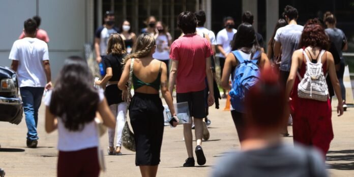 Crowd of students walking away from the camera on a sunny campus walkway, backpacks on their backs.