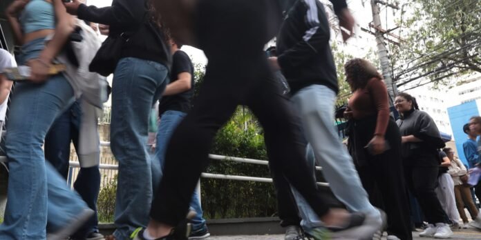 Crowd of people walking quickly along a sidewalk viewed from ground level; motion blur with railing and trees in an urban setting