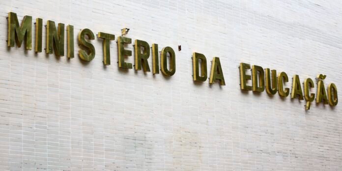 Raised gold letters spell 'MINISTÉRIO DA EDUCAÇÃO' on a pale tiled wall (ministry of education sign).