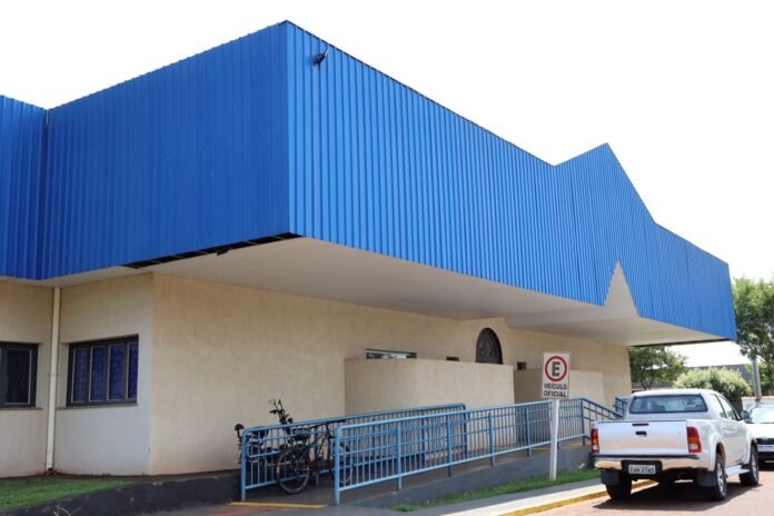 Public building with a bright blue angular roof, beige walls, and a blue railing ramp; a white pickup nearby.