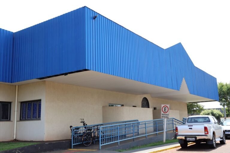 Public building with a bright blue angular roof, beige walls, and a blue railing ramp; a white pickup nearby.