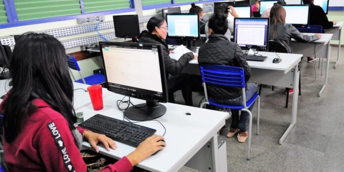 Students working on desktop computers in a computer lab, facing monitors at white desks.
