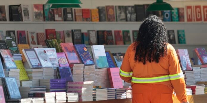 Person in an orange safety jacket browses colorful books at a bookstore display, with stacks of books in front and shelves in the background.