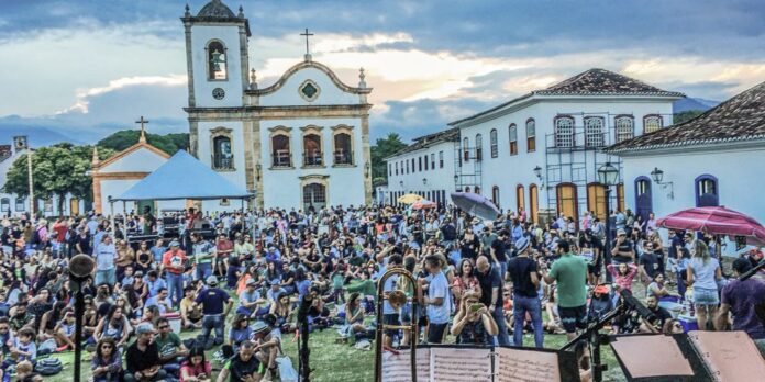 Large crowd gathered in a town square for an outdoor festival in front of a historic church and white colonial buildings.