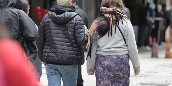 Two people walk away from the camera down a city street in jackets, seen from behind.