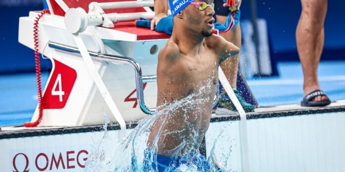 Swimmer emerges from the pool during a race, splashing water as he steps from the starting block labeled 4.
